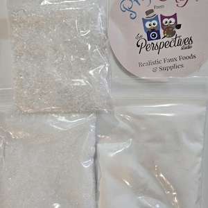 May include: Four clear plastic bags containing various faux food supplies. One bag holds clear, irregular-shaped pieces, while others contain white granular and powdered substances. A circular sticker with the text "Prop Chef" and "Realistic Faux Foods & Supplies" is also visible.