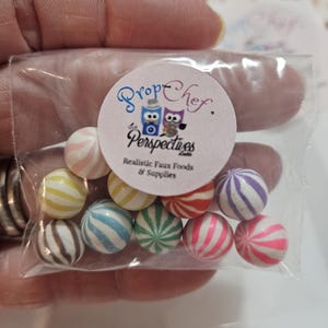 May include: A clear plastic bag filled with colorful, striped faux candies. The candies are various colors, including pink, blue, green, and white. The bag has a circular sticker with the text "Prop Chef Perspectives" and owl illustrations.