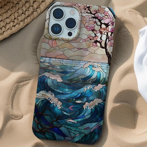 May include: A phone case featuring a stained glass design of a seascape with waves crashing against the shore. The design also includes a tree with pink blossoms and a sunset in the background.