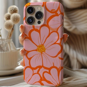 May include: A pink and orange floral phone case with a camera lens cutout. The case features a large pink flower with orange accents and smaller pink flowers surrounding it.