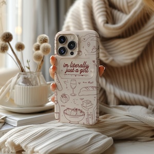 May include: A white phone case with a red and white design. The case features a variety of illustrations, including a glass of wine, a baguette, strawberries, and a heart. The text "im literally just a girl" is written in red on the case.