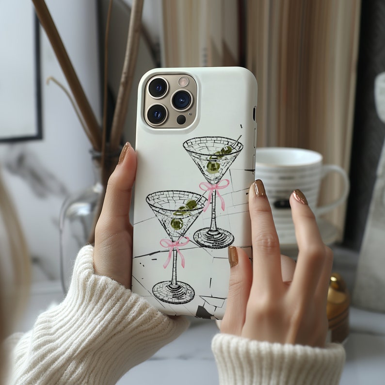 May include: White iPhone case featuring a design of two martini glasses with olives and pink ribbons.