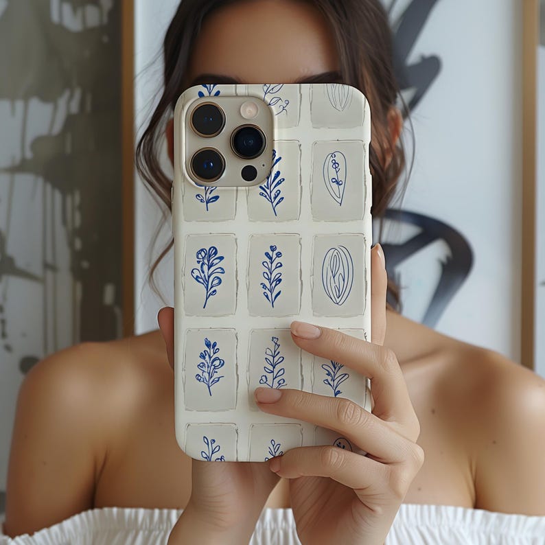 K&ouml;nnte beinhalten: Eine wei&szlig;e iPhone-H&uuml;lle mit einem blauen Blumenmuster. Die H&uuml;lle hat ein Gitterdesign, wobei jedes Quadrat ein anderes Blumenmotiv enth&auml;lt.