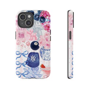 coquette 8 ball collage phone case with graphics like 8 ball, blue berries, hats, ribbons, flowers. phone is perched against a white marble jar with a white background and feathers in the top left corner