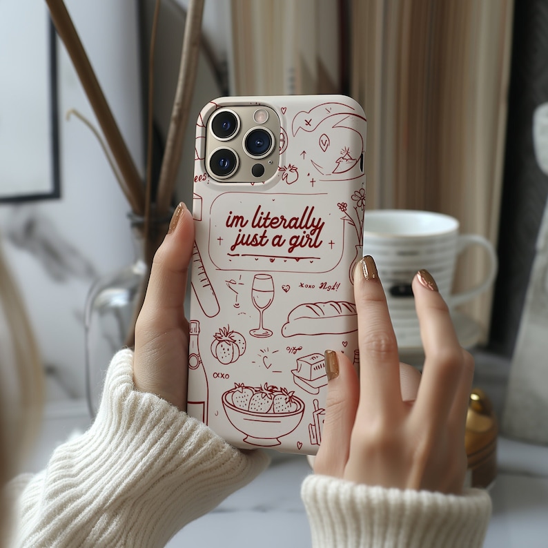 May include: White iPhone case with a red and white design. The design includes a variety of doodles, including a glass of wine, a baguette, strawberries, and a toaster. The text "im literally just a girl" is written in red.