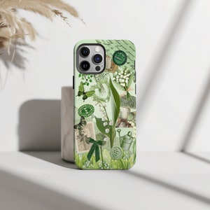 May include: A green and white phone case with a floral design featuring lilies of the valley, butterflies, and a watering can. The case has a vintage aesthetic with a green and white color scheme.