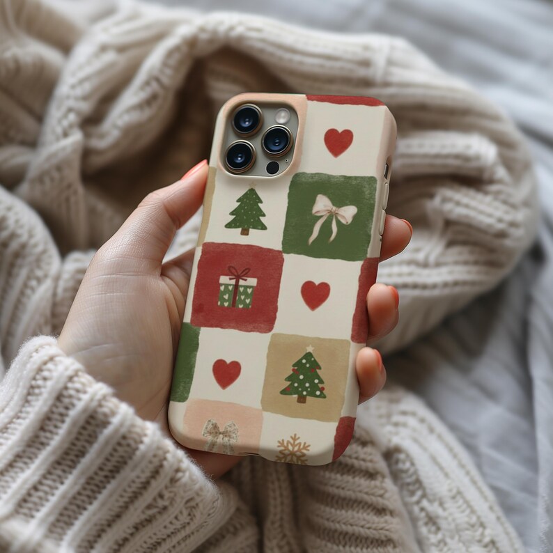 A hand holding a phone case with a Christmas-themed design featuring a Christmas tree, gift boxes, and hearts.