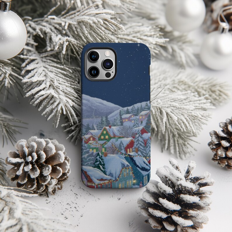 A smartphone case with a winter village scene printed on it, surrounded by pine cones and Christmas ornaments.