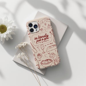 May include: A beige phone case with a doodle design featuring strawberries, wine glasses, bread, and the text "im literally just a girl".
