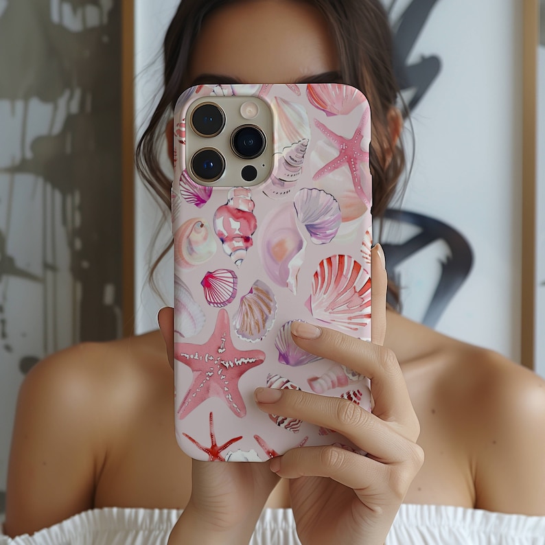 May include: A pink iPhone case with a watercolor design of seashells and starfish. The case has a camera lens cutout and a cutout for the phone's buttons.