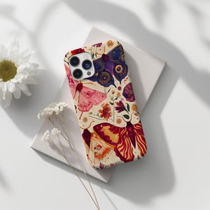 May include: A phone case with a cream background and a colourful pattern of butterflies and flowers. The butterflies are in shades of pink, purple, and orange. The flowers are in shades of red, pink, and yellow.