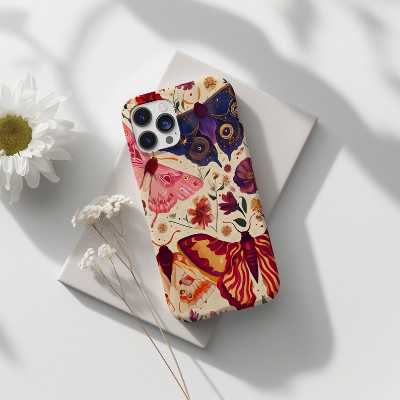 May include: A phone case with a cream background and a colourful pattern of butterflies and flowers. The butterflies are in shades of pink, purple, and orange. The flowers are in shades of red, pink, and yellow.