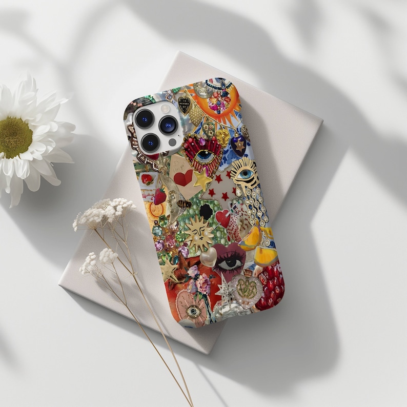 mosaic phone case with elements like jewels, rhinesttones, eyes, pearls, sunm stars and hearts. the phone sits on top of plain white notebook thats framed beautifully with white daisy flowers
