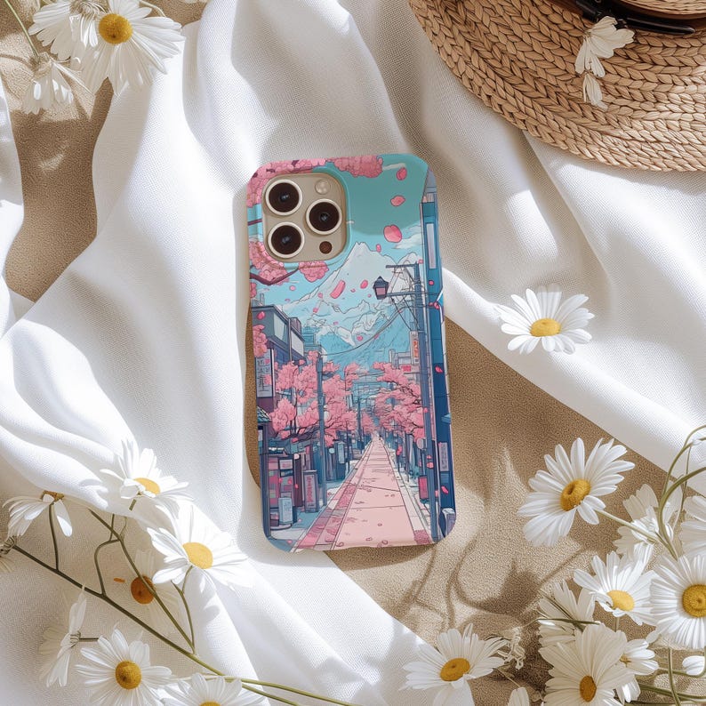 May include: A phone case depicting a Japanese street scene with cherry blossom trees, a mountain, and buildings. The case has a light blue background with pink and purple accents. The case has a camera cutout.