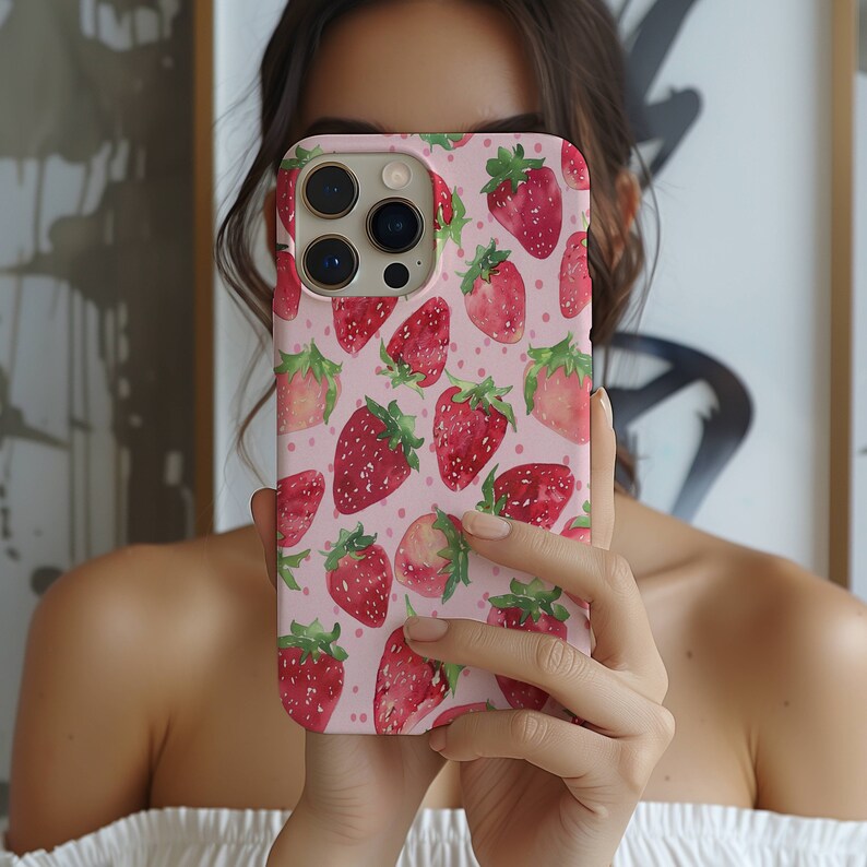 May include: A pink phone case with a watercolour design of strawberries. The case has a white background with pink polka dots and features a variety of strawberries in different sizes and positions.
