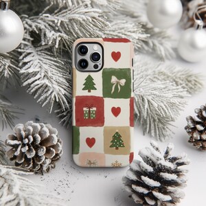 A smartphone case with a Christmas-themed design, featuring a pattern of pine cones, pine branches, and Christmas ornaments, is placed on a snowy surface.
