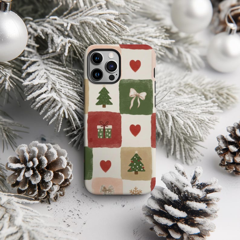 A smartphone case with a Christmas-themed design, featuring a pattern of pine cones, pine branches, and Christmas ornaments, is placed on a snowy surface.