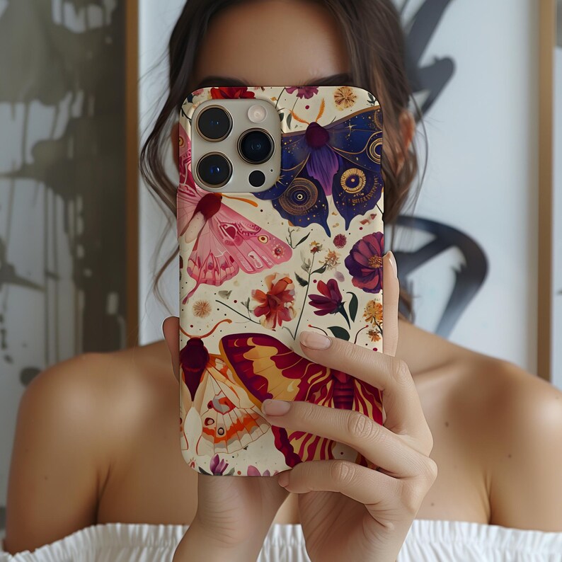 May include: A white iPhone case with a colourful butterfly and floral design. The case features a pink, purple and yellow butterfly with intricate details. The background is a cream colour with a variety of flowers and leaves.