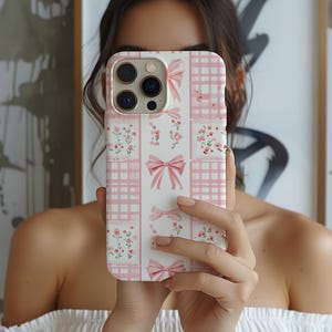 May include: A white phone case with a pink and white checkered pattern, pink bows, and pink flowers.