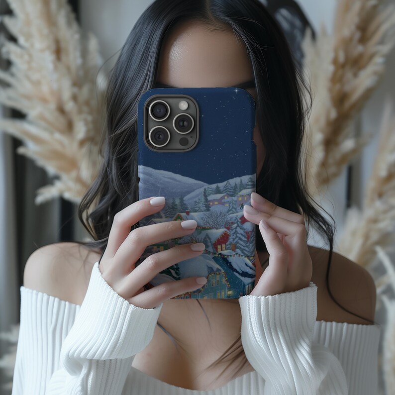 A woman is holding a phone with a picture of a snowy mountain landscape on the case, covering her face as she takes a selfie.