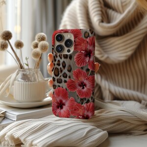 May include: A phone case with a leopard print and red hibiscus flowers. The case has a camera lens cutout and a white background.