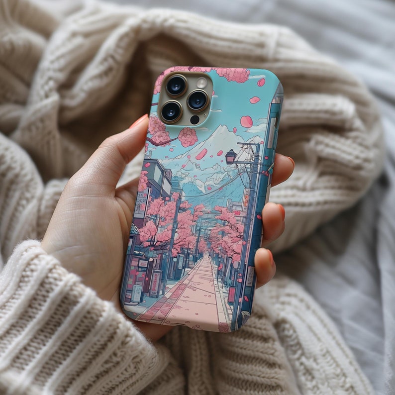 iPhone case featuring a scenic street with cherry blossom trees, falling petals, and a snow-capped mountain in the background. A serene Japanese landscape, perfect for lovers of springtime beauty and tranquil scenes.