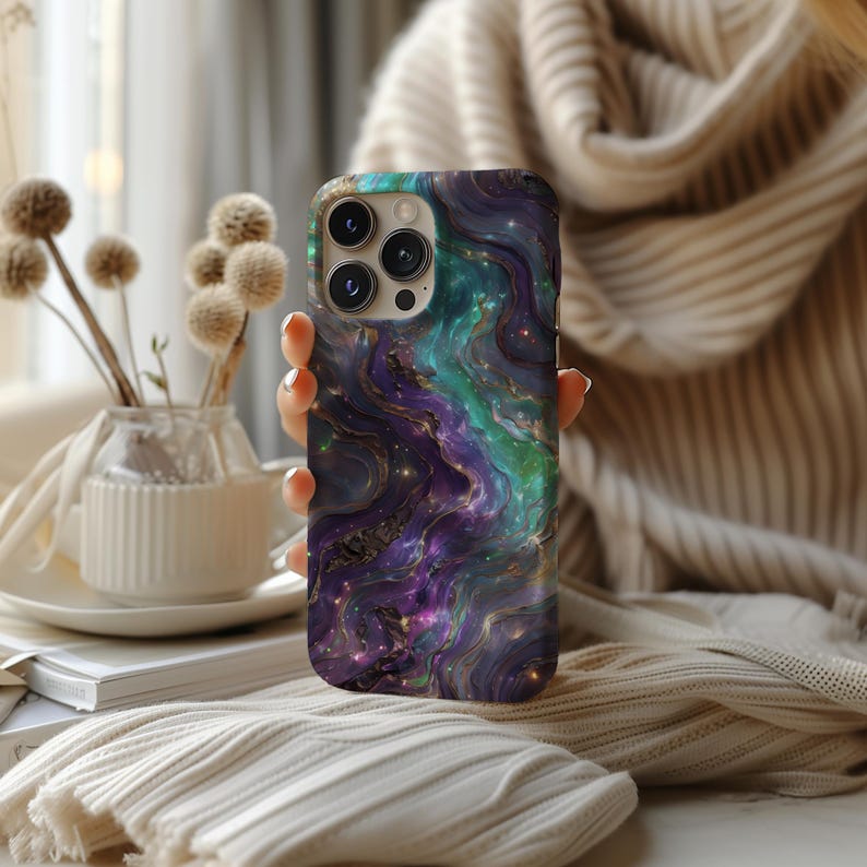 May include: A phone case with a galaxy-like design featuring swirling purple, green, and blue colours with gold accents.