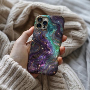 May include: A phone case with a galaxy-inspired design. The case features swirling purple, blue, and green colours with gold accents. The case has a textured surface and a clear camera cutout.