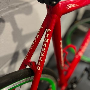 May include: Close-up of a red bicycle frame with white lettering that reads "PINARELLO". The bicycle has a green and silver rim.