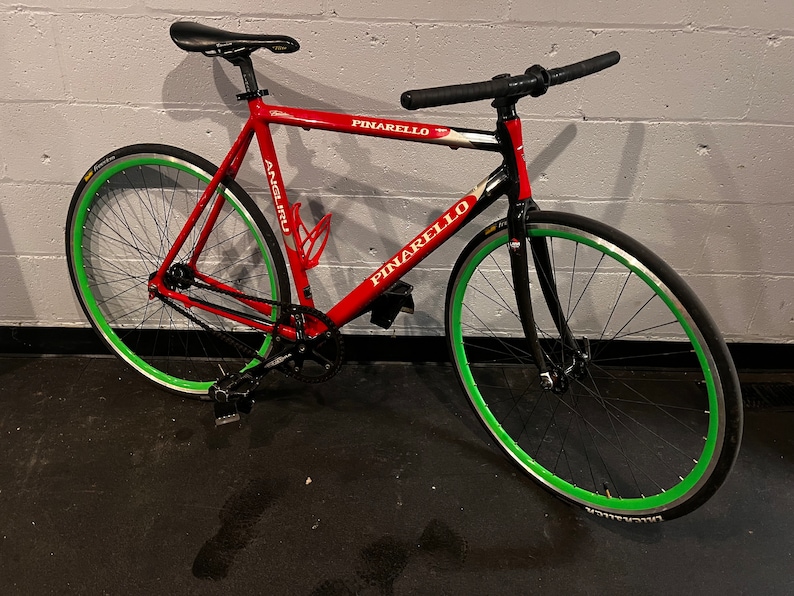 May include: A red Pinarello road bike with black handlebars and green wheels. The bike has a white Pinarello logo on the frame.