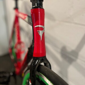 May include: A red and black bicycle frame with a silver logo. The frame is made of carbon fiber and has a green rim.