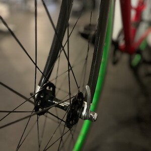 May include: Close-up of a black bicycle wheel with a green rim and a silver quick-release lever.