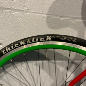 May include: Close-up of a bicycle wheel with a black tire and green rim. The tire has the words "ThickSlick" and "Urban Armor Casing" printed on it.
