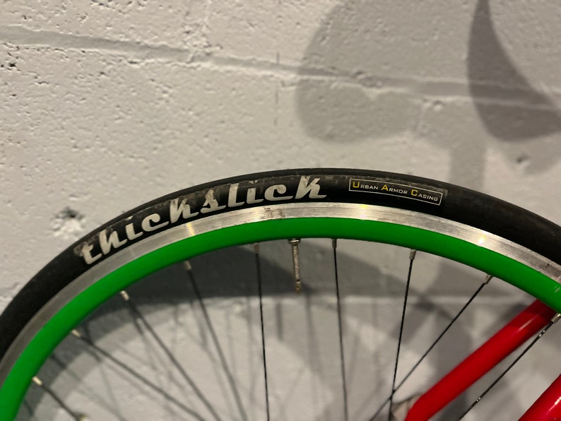 May include: Close-up of a bicycle wheel with a black tire and green rim. The tire has the words "ThickSlick" and "Urban Armor Casing" printed on it.