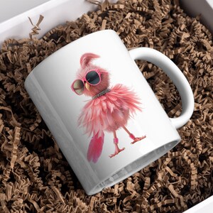 May include: White ceramic mug with a pink flamingo wearing sunglasses and a sparkly necklace. The flamingo is standing on one leg and has its wings spread out. The mug is in a box with brown packing paper.