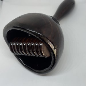 Puede incluir: Un rodillo de madera marrón oscuro con un mango. El rodillo tiene una serie de pequeñas piezas redondas de madera que están unidas a un eje central.