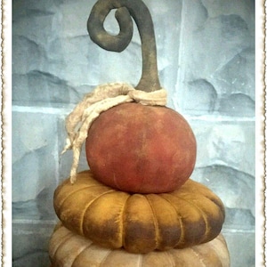 May include: A stack of four fabric pumpkins in various shades of orange and brown. The top pumpkin has a curled stem and a white fabric ribbon.