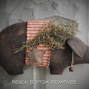 May include: A brown fabric pig ornament with a red and white striped fabric ribbon and a star-shaped tag that says "PIG". The pig has a bell hanging from its ear and is decorated with dried flowers.