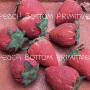 May include: Eight red fabric strawberries with green leaves, arranged on a brown surface. The strawberries are handmade and have a rustic, vintage look. The text "Peach Bottom Primitives" is visible in the image.