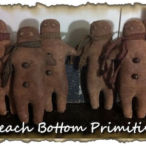 May include: Five brown gingerbread people dolls with brown and red plaid scarves. The dolls are standing in a row on a dark surface. The text "Peach Bottom Primitives" is at the bottom of the image.
