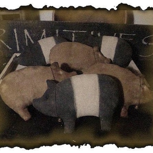 May include: Three primitive style pig figurines, painted in black and white stripes and brown. The figurines are arranged in a stack, with the top pig's head tilted to the side. The word "PRIMITIVES" is written on a chalkboard behind the figurines.