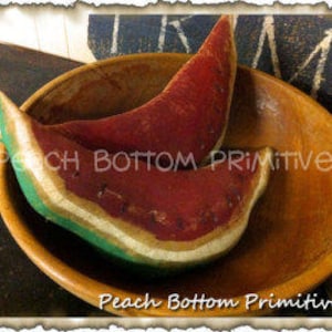 May include: Two red and green felt watermelon slices in a wooden bowl. The watermelon slices are handmade and have a rustic, primitive style.