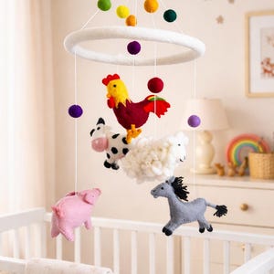 May include: A baby crib mobile featuring felt farm animals: a rooster, cow, sheep, pig, and horse. The mobile has a white ring with colorful felt balls and is suspended above a white crib with a star-patterned blanket.