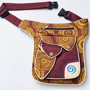 May include: A burgundy and yellow floral patterned hip bag with an adjustable strap and black plastic buckle. The bag features a zipped main compartment, two front flap pockets with gold-tone snap buttons, and a blue embroidered spiral design.