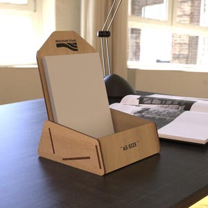 Puede incluir: Un expositor de folletos de madera clara, con papel blanco. Está etiquetado como "A5 SIZE" y "BROCHURE STAND". Se encuentra sobre un escritorio oscuro, junto a un libro abierto.