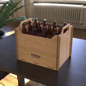 Puede incluir: Una caja de cerveza de madera clara con asa, que contiene doce botellas de vidrio marrón. La caja tiene el texto "WOODIN 12 BEER BOX" impreso en el lateral. La caja está sobre una mesa oscura.
