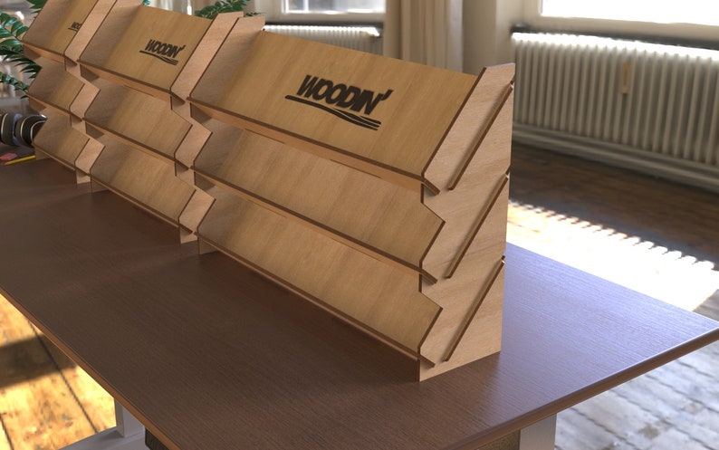 May include: A wooden display stand with five shelves, angled to create a cascading effect. The stand is made of light brown wood and features the logo "WOODIN" on the top shelf.