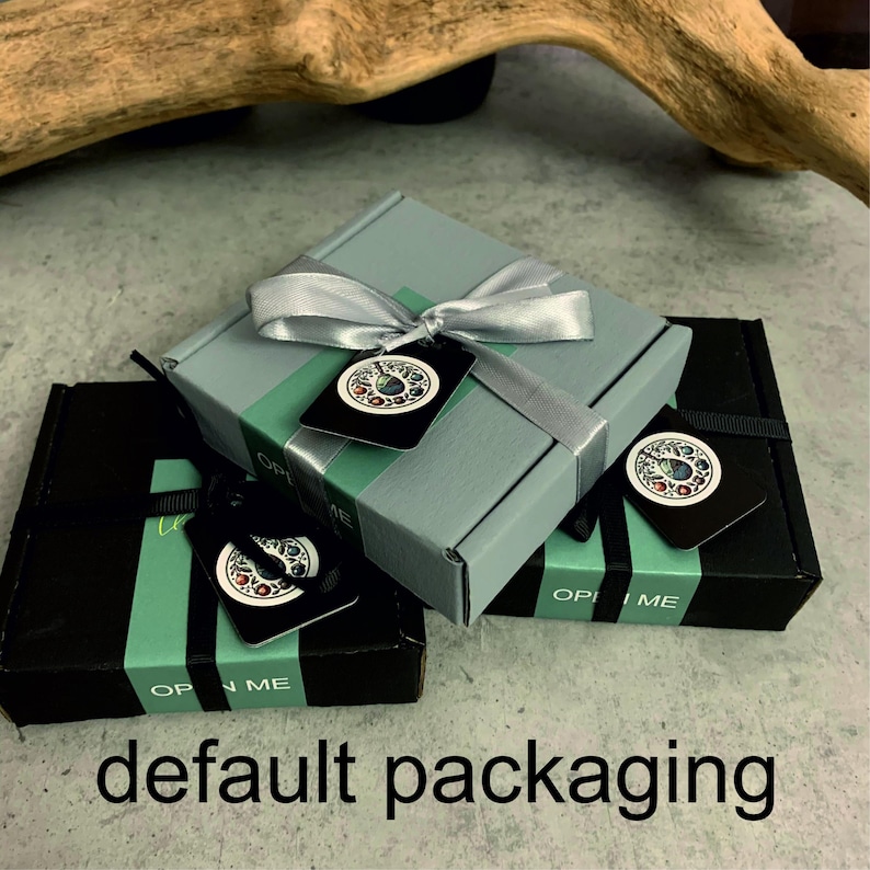 May include: Three gift boxes, two black and one gray, are stacked. Each box is tied with a ribbon and has a decorative tag. The tags and boxes have the words "OPEN ME" printed on them. The text "default packaging" is at the bottom.