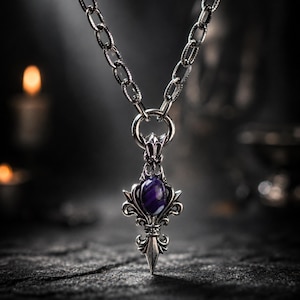 May include: A silver-toned metal necklace featuring a thick, textured chain and a pendant with an ornate, pointed design. The pendant is centred with a smooth, oval-shaped purple stone and is suspended from a circular metal ring bail.