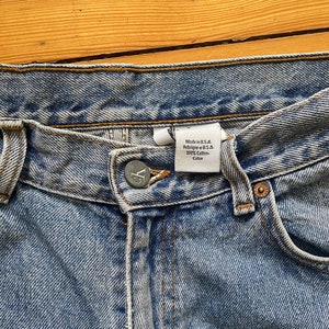 Könnte beinhalten: Nahaufnahme der Bundweite einer hellblauen Jeans. Die Jeans hat einen Knopfverschluss und ein Etikett mit der Aufschrift "Made in U.S.A. - Fabrique au U.S.A. - 100% Cotton - Coton".